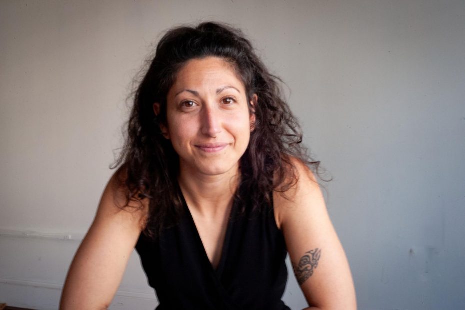 IMAGEN de 3/4 de una mujer sonriente con cabello y chaleco oscuro